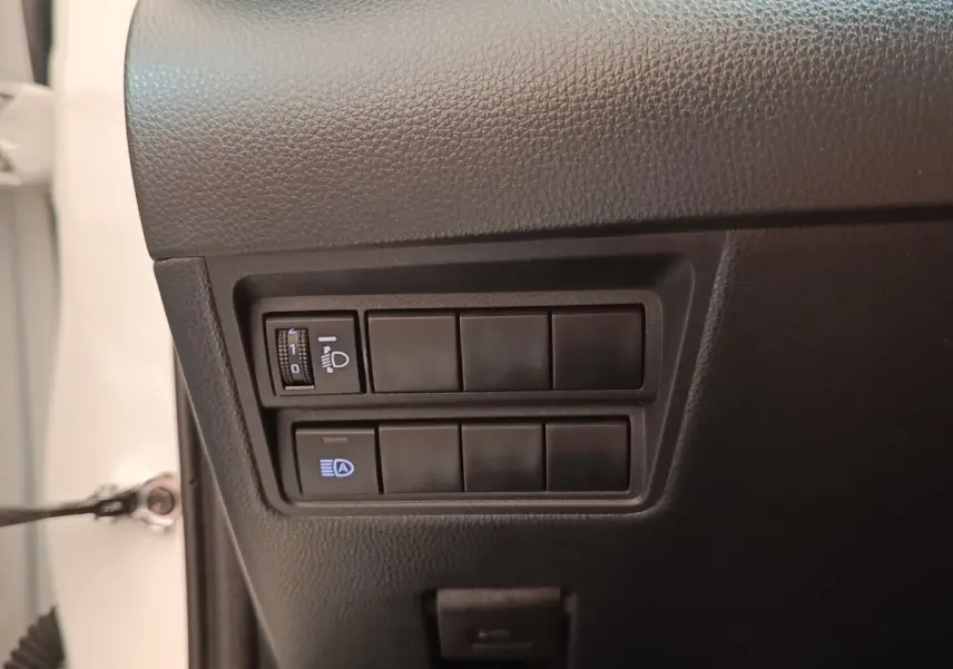Détail intérieur montrant les commandes de réglage des phares sur la Toyota Yaris blanche hybride 2022.