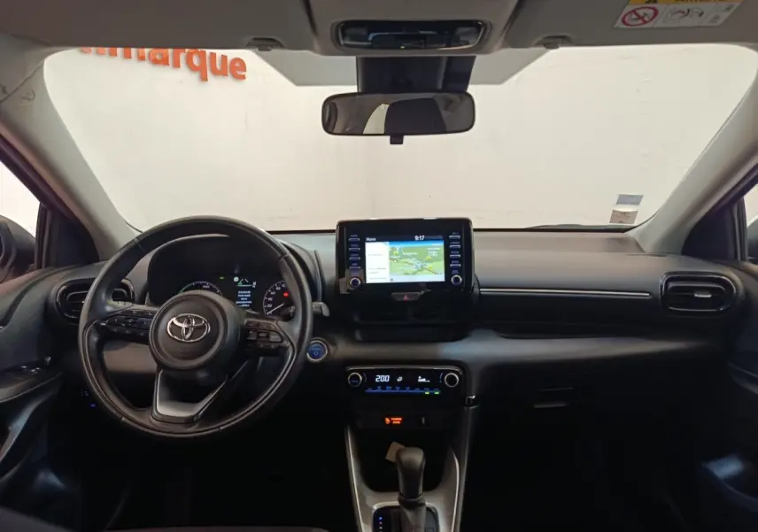 Vue intérieure avant du tableau de bord noir d'une Toyota Yaris hybride 2022 avec écran tactile central et volant cuir multifonctions.