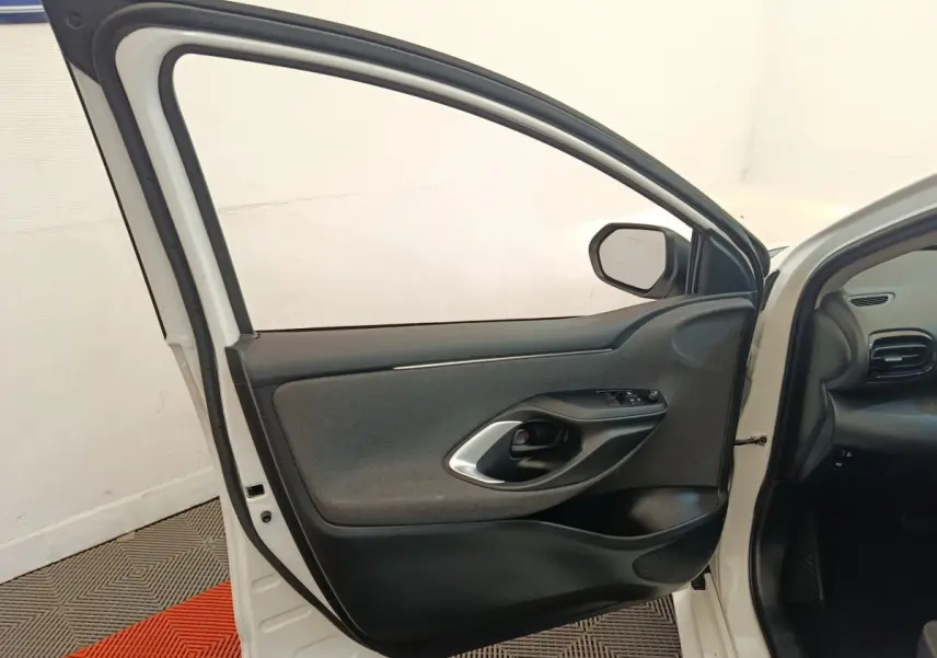Vue intérieure de la porte avant gauche ouverte d’une Toyota Yaris blanche, montrant la garniture noire et grise.
