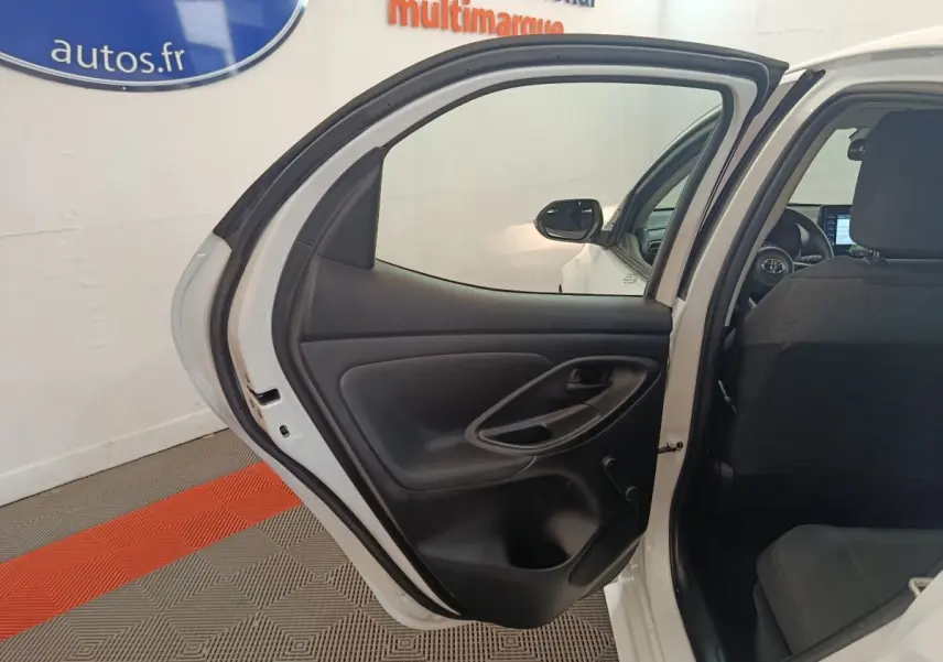 Vue intérieure sur la porte arrière gauche ouverte d'une Toyota Yaris blanche 2022, avec siège arrière et tableau de bord partiellement visibles.