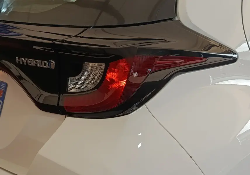 Gros plan sur le feu arrière droit noir et rouge d'une Toyota Yaris hybride blanche, avec logo Hybrid visible.