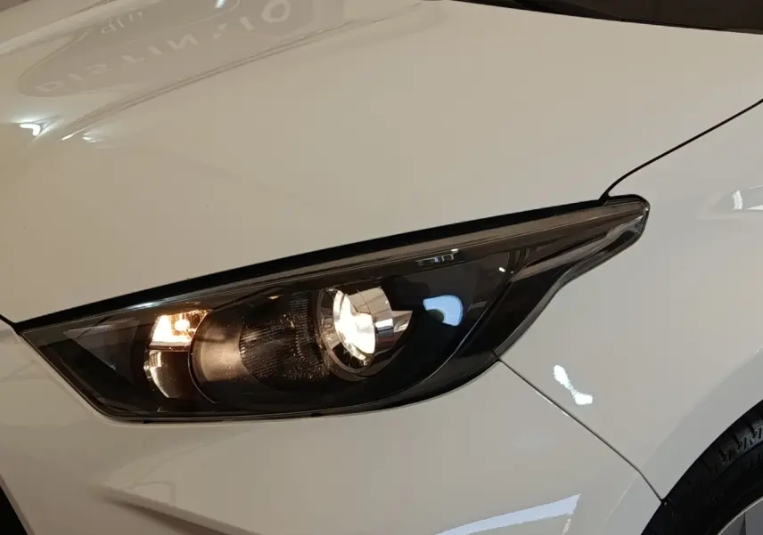 Gros plan sur le phare avant droit allumé d'une Toyota Yaris blanche, soulignant les lignes épurées du capot.