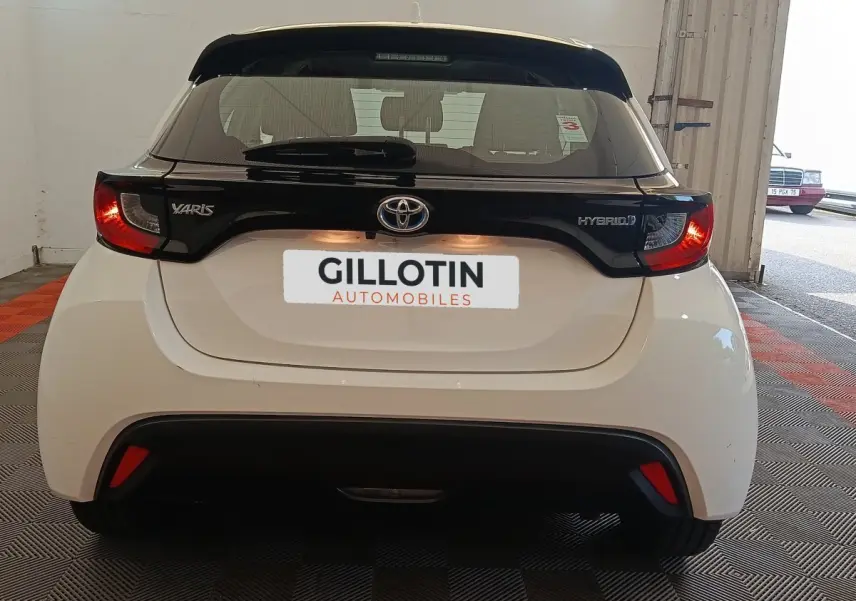 Vue arrière de la Toyota Yaris hybride blanche 2022 avec spoiler noir et feux arrière allumés dans un garage.