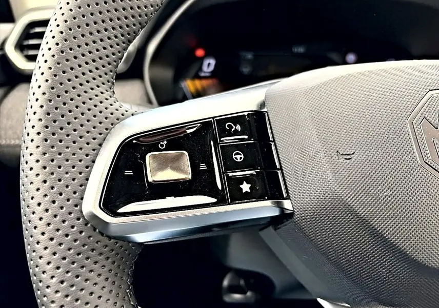Gros plan sur la partie gauche du volant perforé gris avec commandes multifonctions du MG MOTOR ZS hybride 2026.