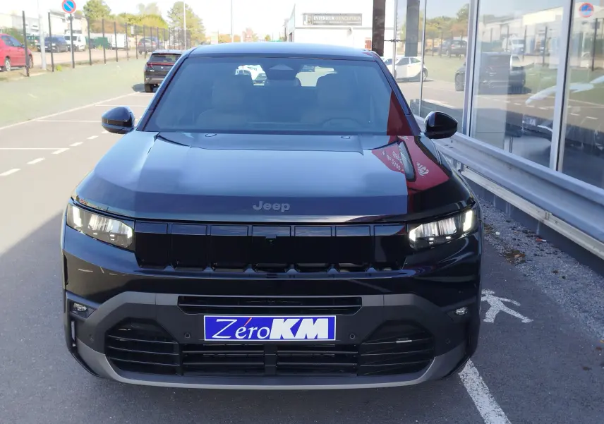 Vue avant d'un Jeep Compass noir Vulcano métallisé, avec calandre noire et phares LED allumés, stationné devant un bâtiment vitré.