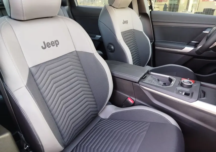 Vue intérieure rapprochée des sièges avant gris clair et noir du Jeep Compass 2026 avec logo brodé et console centrale moderne.