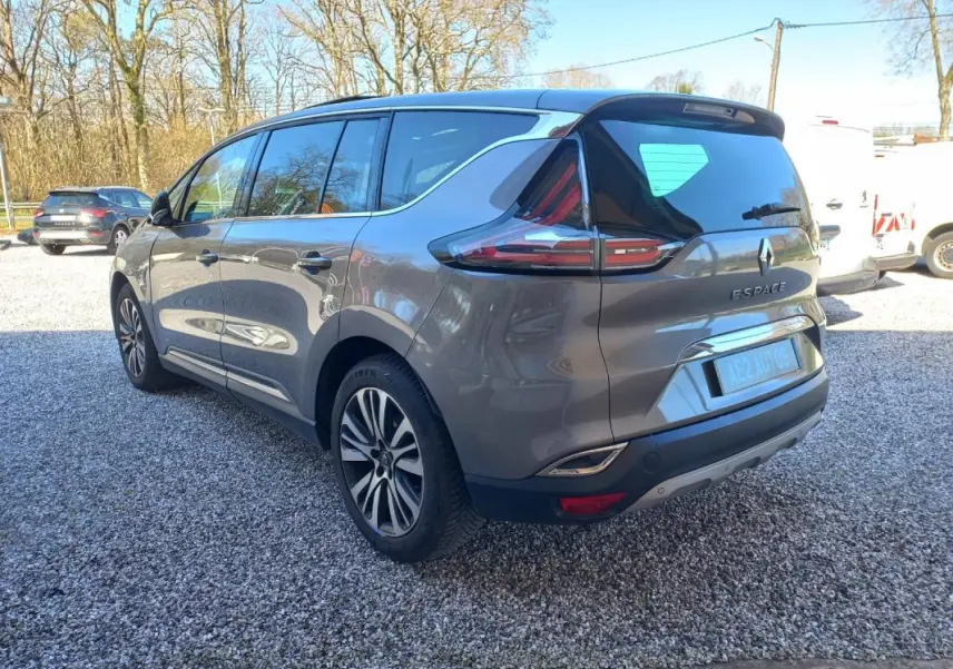 Renault Espace gris vue 3/4 arrière droit, avec feux arrière distinctifs et jantes alliage, stationné sur gravier.