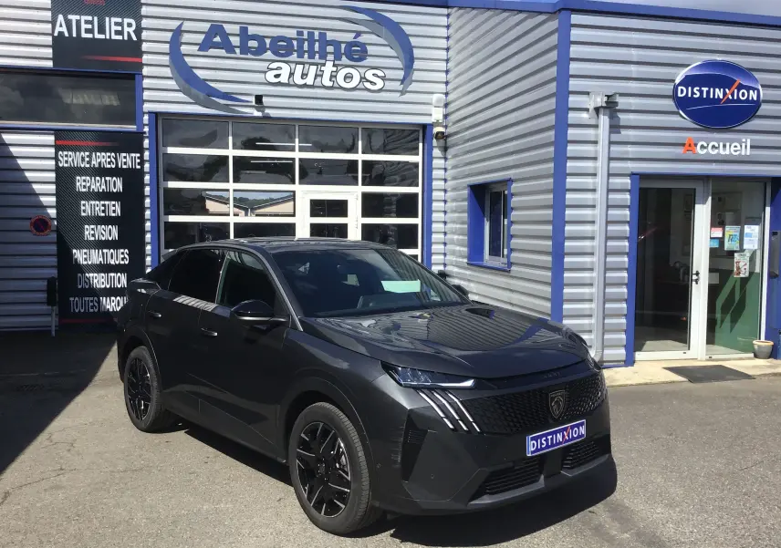 Peugeot 3008 gris titane en 3/4 avant droit, avec calandre noire et jantes alliage noires devant un garage automobile.