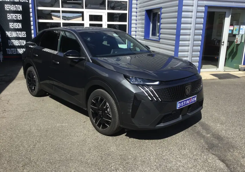 Peugeot 3008 gris titane en 3/4 avant droit, avec calandre noire et jantes alliage noires, garée devant un atelier.