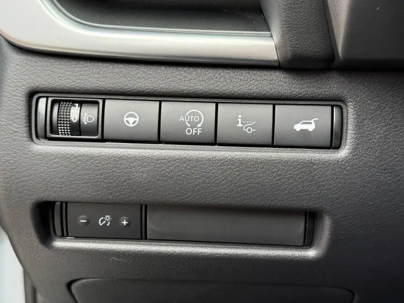 Gros plan sur les commandes noires du tableau de bord du Nissan Qashqai 2025, boutons de réglages et ouverture coffre.