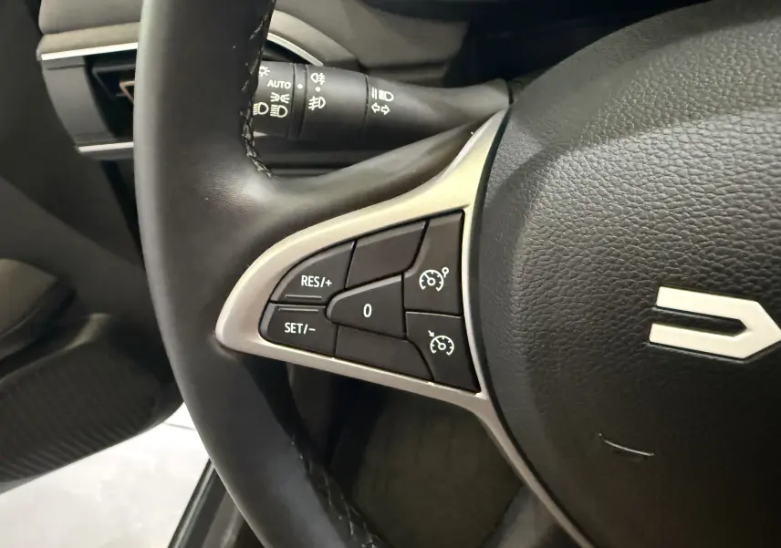 Gros plan sur les commandes de régulateur de vitesse à gauche du volant noir du Dacia Jogger Hybrid 140 Extreme 2023.