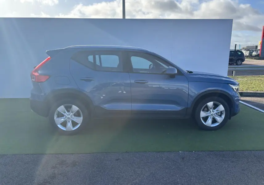 Profil côté droit d'un Volvo XC40 2024 Fjord Blue Metal avec jantes alliage 18 pouces sur fond clair.