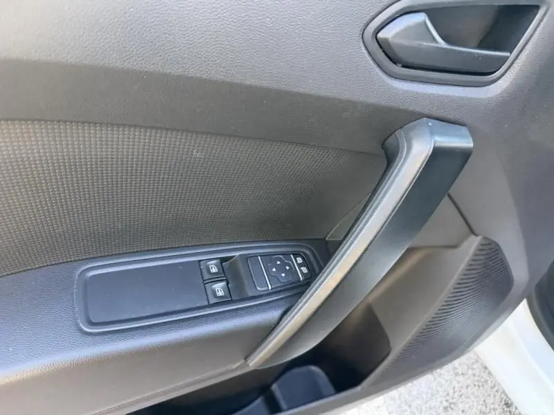 Gros plan sur la porte avant gauche du Renault Kangoo blanc 2022, montrant les commandes électriques des vitres et la poignée intérieure.