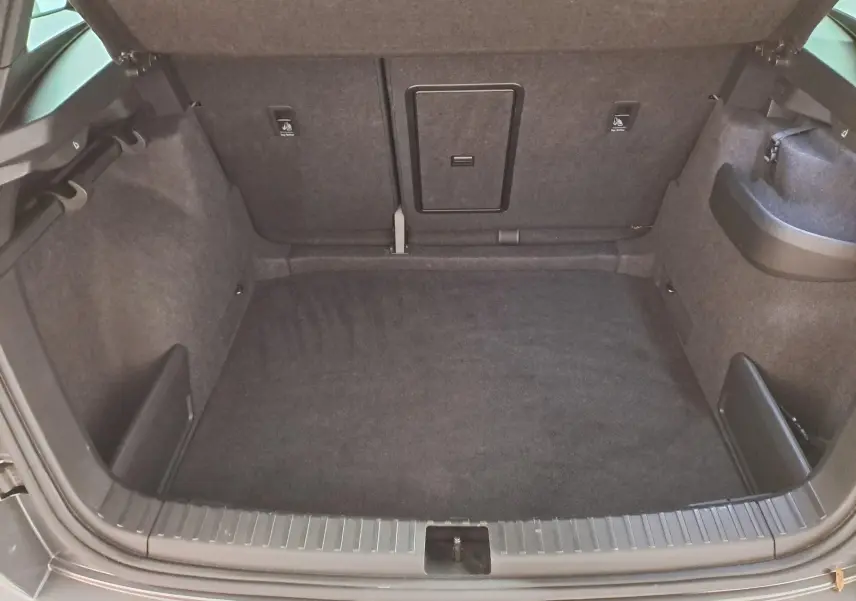 Coffre ouvert vu de l'arrière d'un Skoda Karoq gris graphite 2025, avec revêtement intérieur sombre et hayon électrique.
