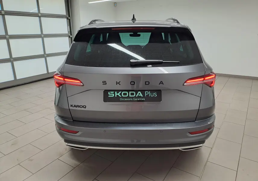 Vue arrière d'un Skoda Karoq gris graphite 2025 avec feux allumés et hayon électrique en intérieur showroom.