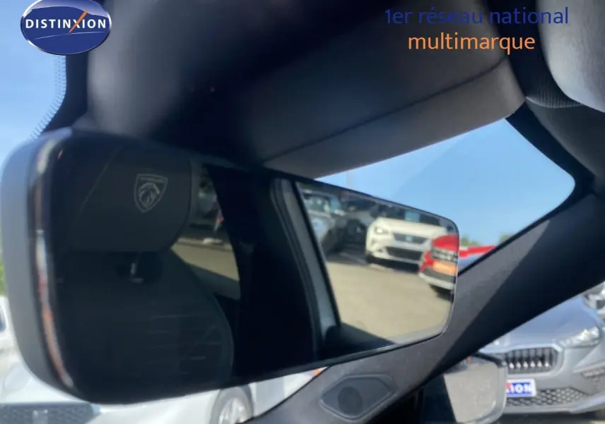 Rétroviseur intérieur montrant le siège noir avec logo Peugeot, reflet d’un parking extérieur avec plusieurs voitures visibles.