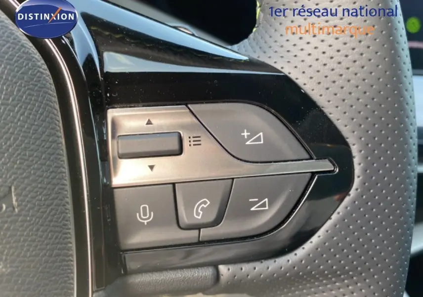 Gros plan sur les commandes multifonctions côté gauche du volant perforé d’une Peugeot 308 Hybrid blanche.