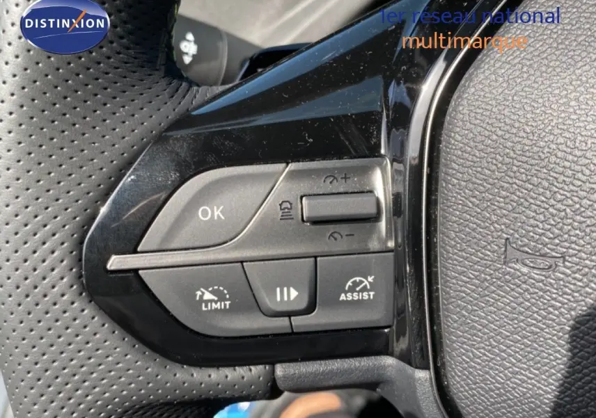 Gros plan sur les commandes de régulateur de vitesse au volant noir perforé d’une Peugeot 308 Hybrid blanche.