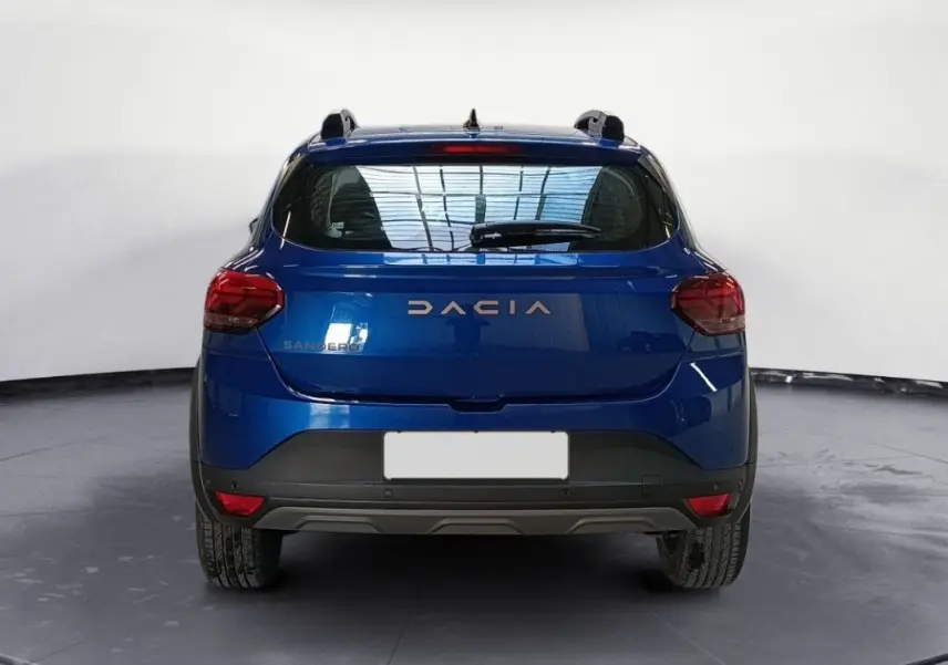 Vue arrière d'une Dacia Sandero Stepway 2025 en bleu Iron, avec feux arrière rouges et toit équipé de barres de toit.