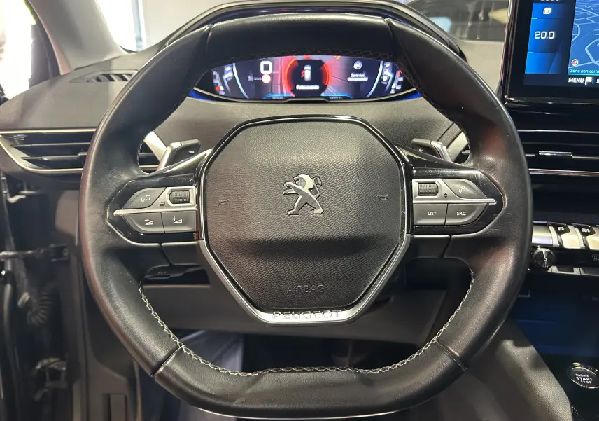 Vue rapprochée du volant cuir noir du Peugeot 3008 II Ph.2 avec commandes intégrées et tableau de bord numérique en arrière-plan.