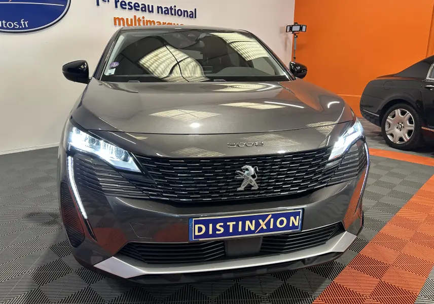 Vue avant d'un Peugeot 3008 gris Platinium avec phares LED allumés et calandre noire distinctive en showroom.