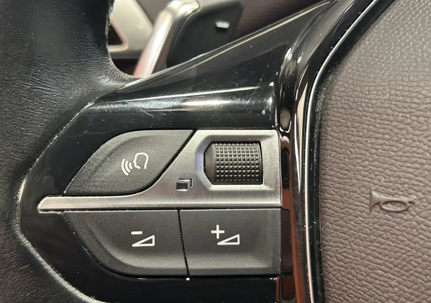 Gros plan sur les commandes de volume et téléphone intégrées au volant cuir noir du Peugeot 3008 gris Platinium.