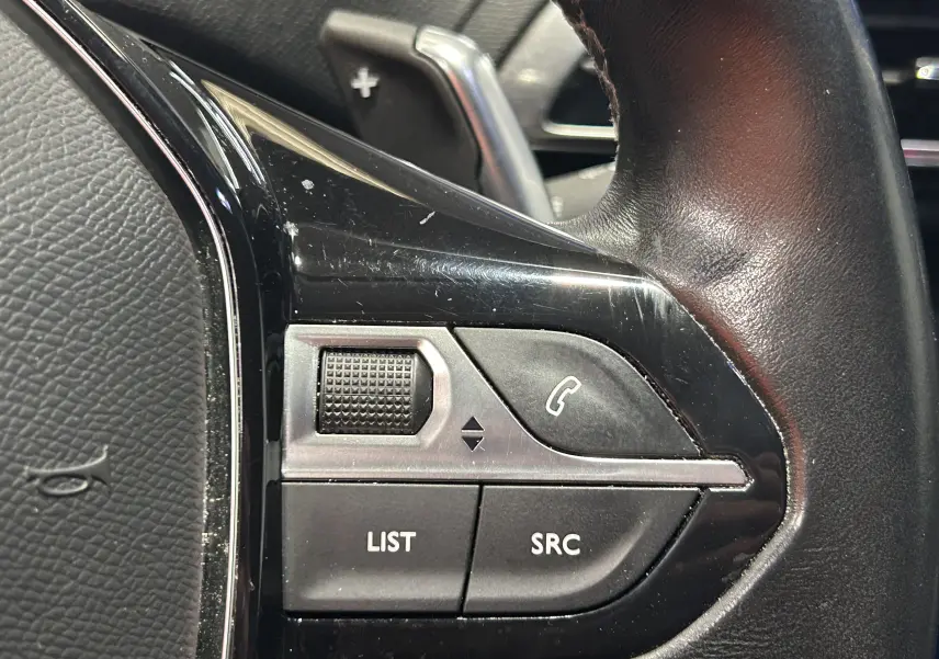 Gros plan sur les commandes gauche du volant en cuir noir du Peugeot 3008, boutons de gestion d’appels et audio.
