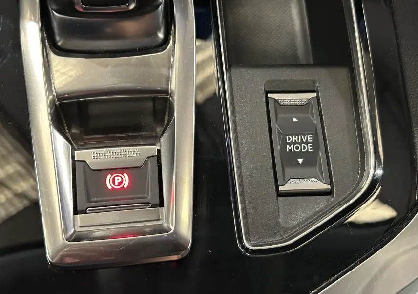 Gros plan sur la console centrale noire brillante du Peugeot 3008 avec bouton frein à main électronique et sélection Drive Mode.