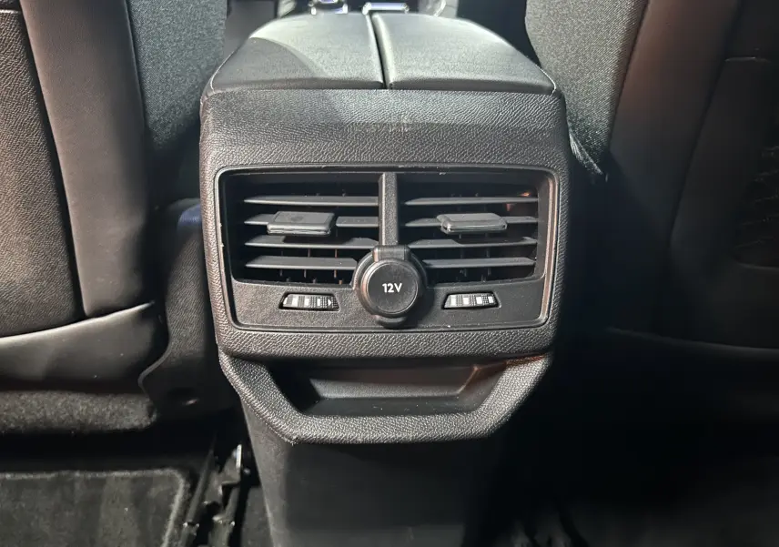 Gros plan sur la console centrale arrière noire du Peugeot 3008 II Ph.2 avec prises d'air et prise 12V visible.