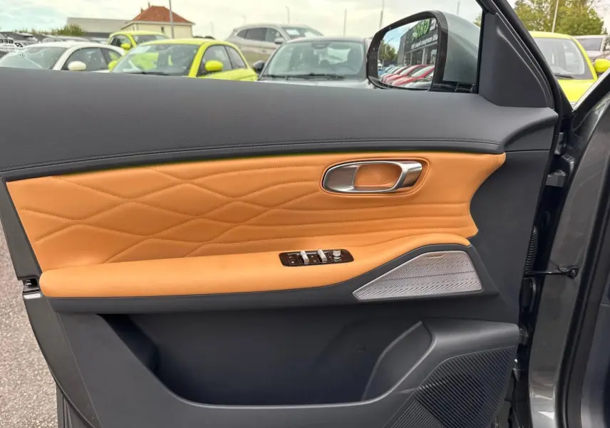 Vue intérieure côté gauche de la porte d’une Geely STARRAY 1.5 EM-i 262ch Max+ en Volcanic Grey avec garniture cuir marron et haut-parleur Harman Kardon.