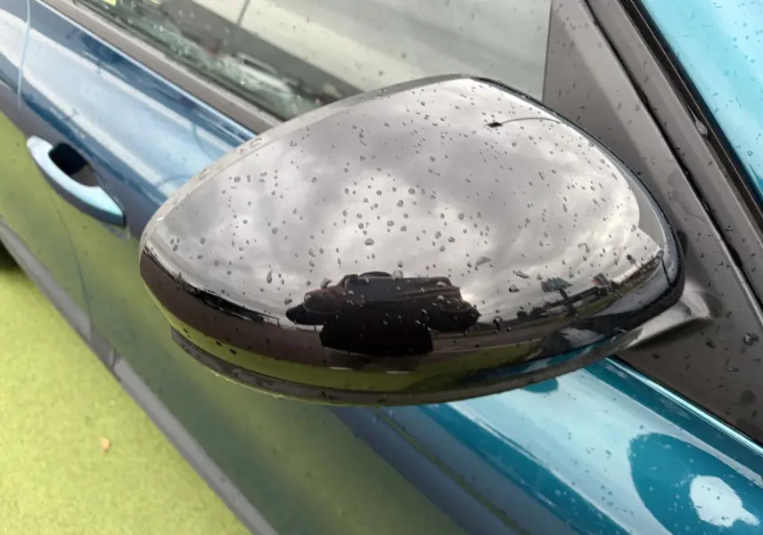Gros plan sur le rétroviseur noir brillant côté gauche d'une Renault Arkana bleu Zanzibar métallisé avec gouttes de pluie.