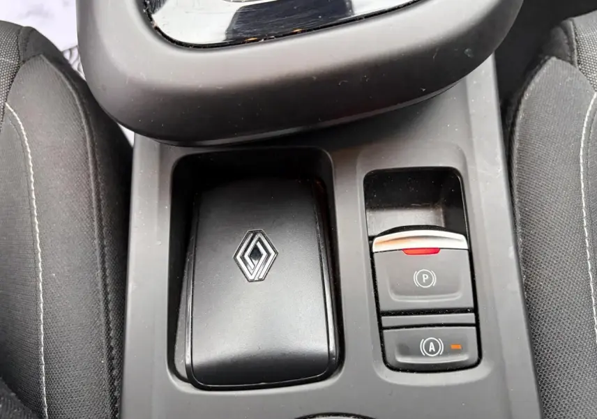 Gros plan sur la console centrale noire avec logo Renault et commandes de frein de parking et auto-hold du Renault Arkana.