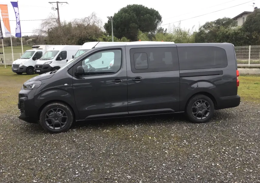 Vue de profil côté gauche du FIAT Scudo Combi gris titane avec vitres latérales coulissantes sur un sol gravillonné.