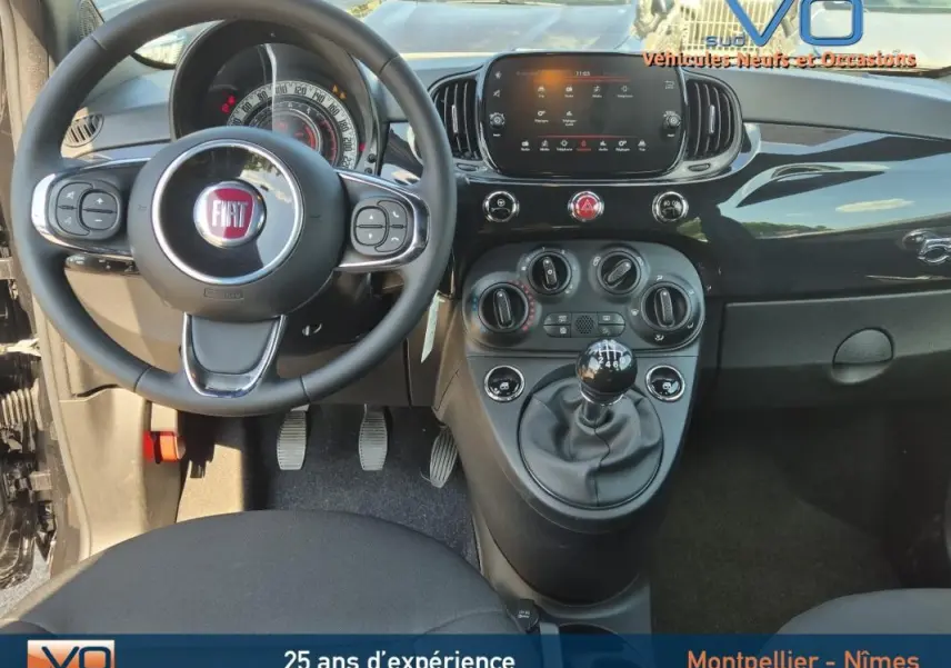 Vue intérieure avant de la Fiat 500C noire 2024, avec volant multifonction, tableau de bord digital et levier de vitesse manuel.