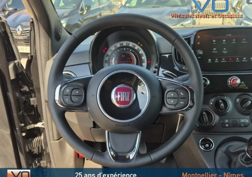 Vue intérieure centrée sur le volant noir de la FIAT 500C 2024 avec tableau de bord et commandes visibles.