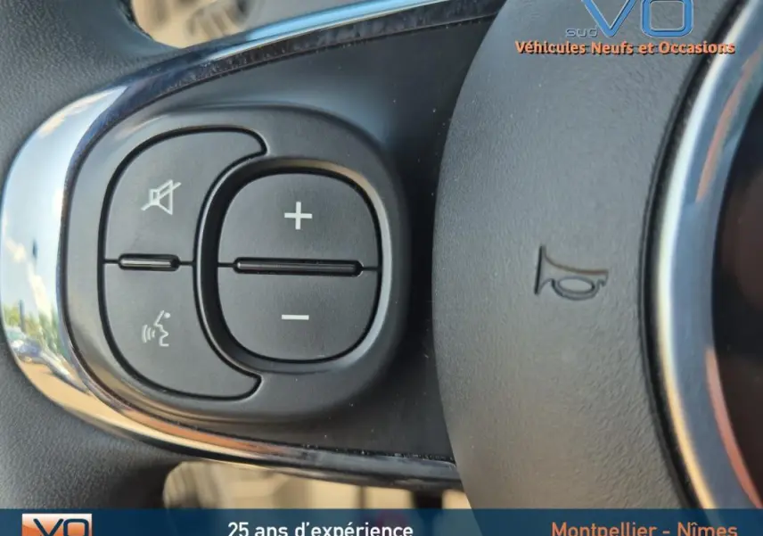 Gros plan sur les commandes de volume et de téléphone au volant noir de la FIAT 500C 2024 hybride.