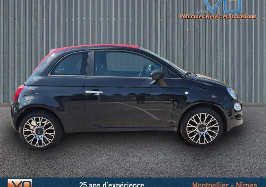 Profil côté gauche de la FIAT 500C noire 2024 avec toit rouge et jantes alliage 15 pouces, sur fond industriel.