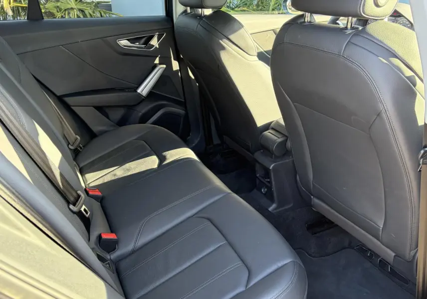 Vue intérieure arrière côté gauche de l'Audi Q2 35 TFSI S-Line 2024 avec sièges en cuir noir et finitions modernes.