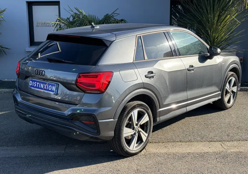 Audi Q2 gris Daytona en vue 3/4 arrière droit, avec jantes alliage 18 pouces et vitres arrière surteintées.