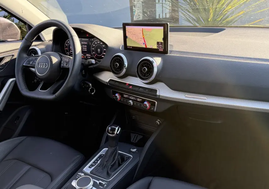 Vue intérieure côté conducteur de l'Audi Q2 2024, tableau de bord avec écran GPS et volant cuir multifonction.
