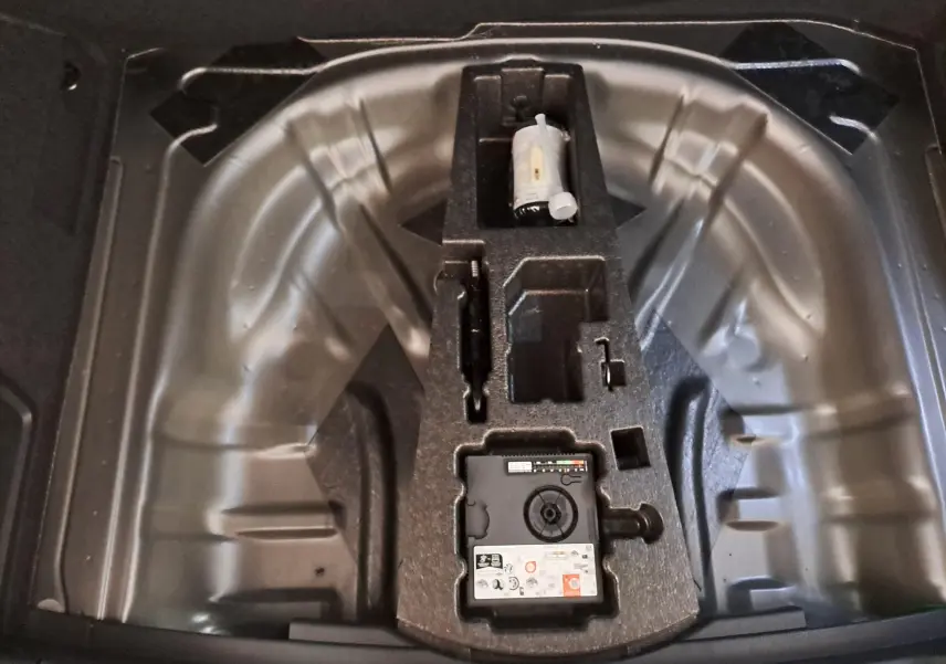 Coffre ouvert du Skoda Karoq gris graphite montrant le rangement pour roue de secours et kit de réparation.