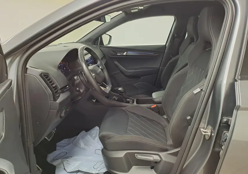 Vue intérieure côté conducteur du Skoda Karoq gris graphite 2025, sièges sport avec surpiqûres blanches et tableau de bord moderne.