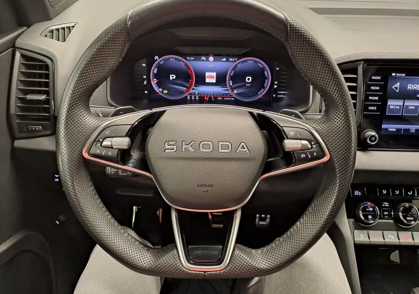Vue rapprochée du volant perforé SKODA KAROQ 2.0 TDI 150 DSG7 SPORTLINE avec tableau de bord numérique et commandes intégrées.