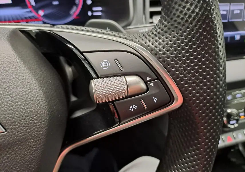 Gros plan sur les commandes gauche du volant perforé du Skoda Karoq 2025, avec molette et boutons noirs.
