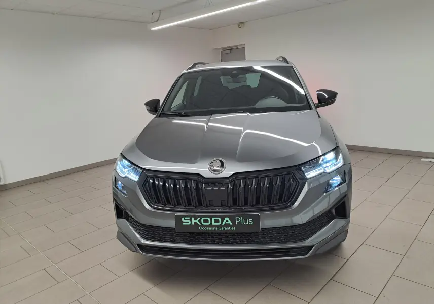 Vue frontale d'un Skoda Karoq gris graphite 2025 avec phares allumés et calandre noire sportive.