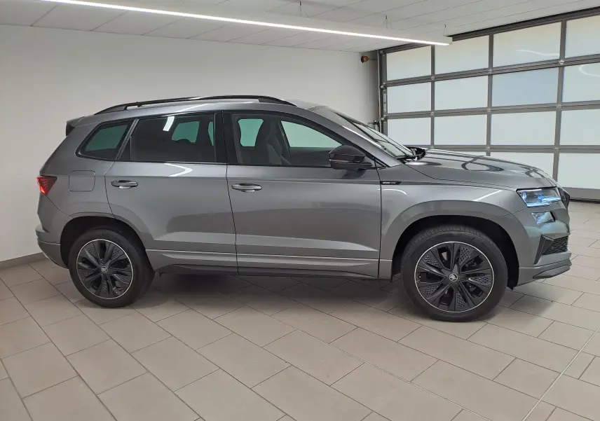 Vue de profil côté gauche du Skoda Karoq 2025 gris graphite avec jantes noires et toit ouvrant en intérieur showroom.