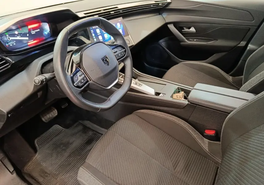 Vue intérieure côté conducteur de la Peugeot 308 2023, avec volant cuir, tableau de bord digital et sièges noirs.