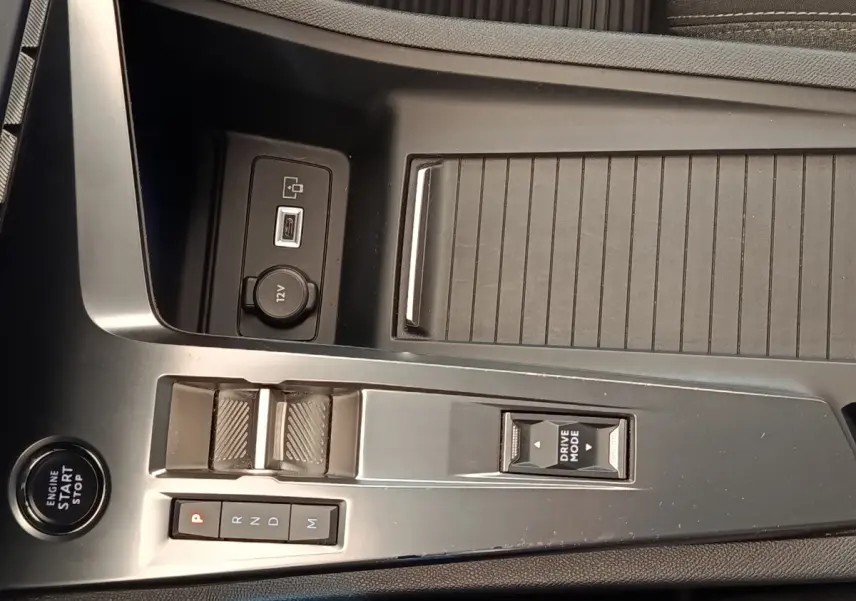 Vue rapprochée de la console centrale noire du Peugeot 308 2023 avec bouton start, sélecteur de mode et prise 12V.