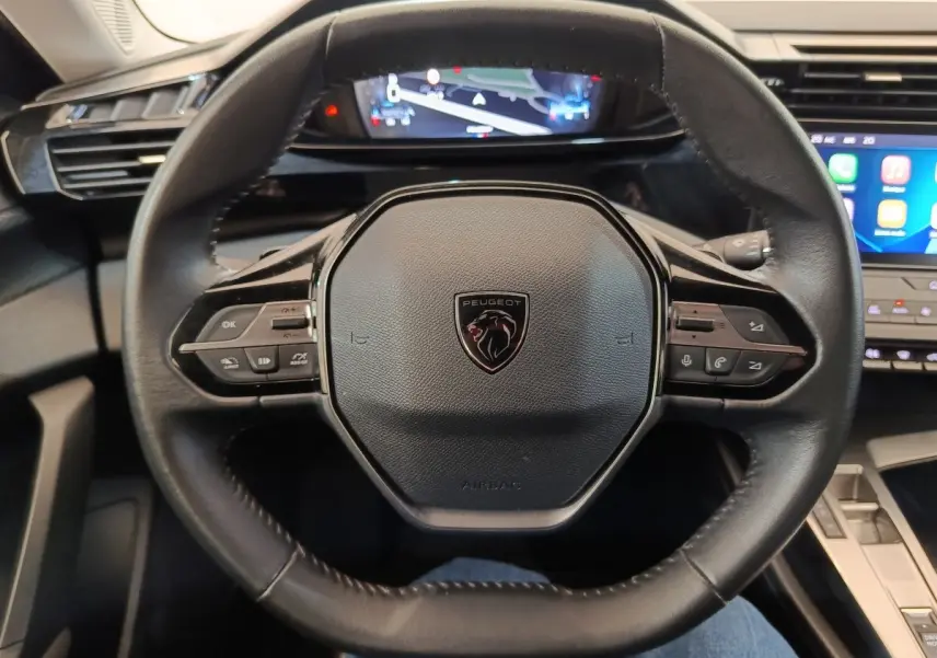 Vue rapprochée du volant cuir noir de la Peugeot 308 2023 avec commandes multifonctions et tableau de bord digital.