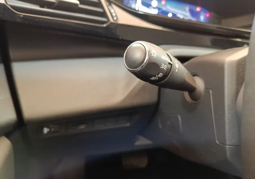 Gros plan sur la commande de phares noire à gauche du volant dans l’habitacle gris foncé du Peugeot 308 2023.